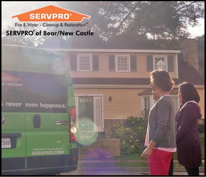 Two woman stand in front of yellow house looking at a parked SERVPRO van